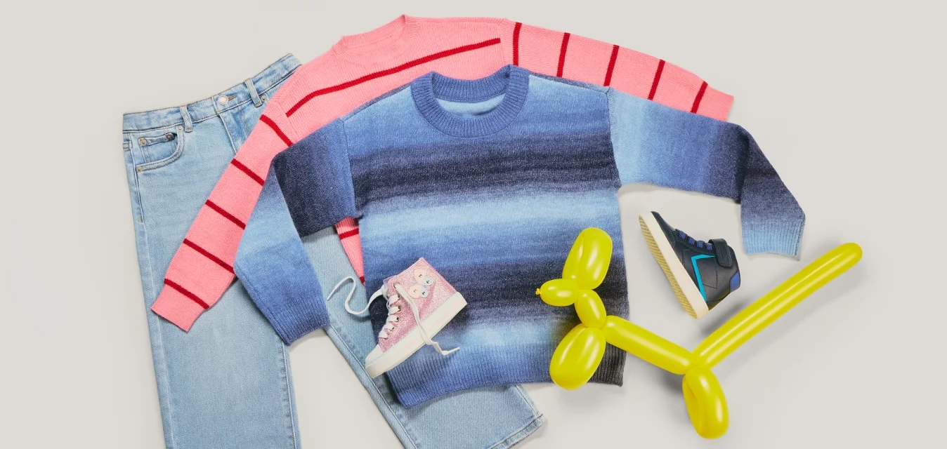 Due paia di jeans, un maglione a righe rosa, un maglione a gradiente blu, due paia di scarpe da ginnastica e un cane a palloncino giallo su uno sfondo chiaro.