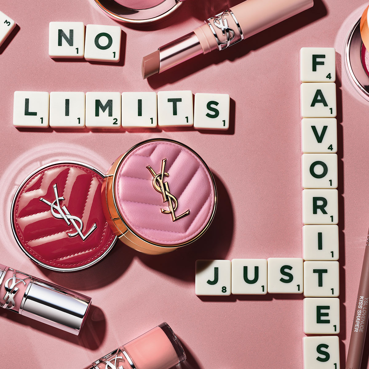 Una selezione di cosmetici rosa YSL disposti con tessere di Scrabble che compongono "NO LIMITS, JUST FAVORITES" su sfondo rosa.