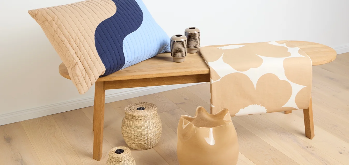 Un tavolo di legno marrone sostiene un cuscino imbottito blu e beige, una coperta beige con motivo, due vasi in ceramica testurizzati e cestini intrecciati.