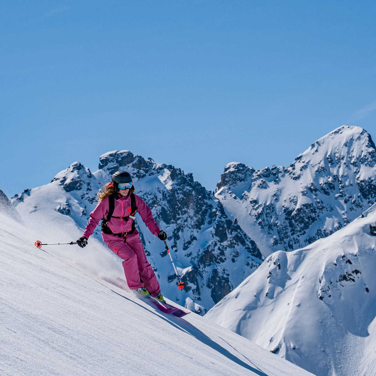 Woman skiing in a pink Helly Hansen outfit on a snowy mountain.