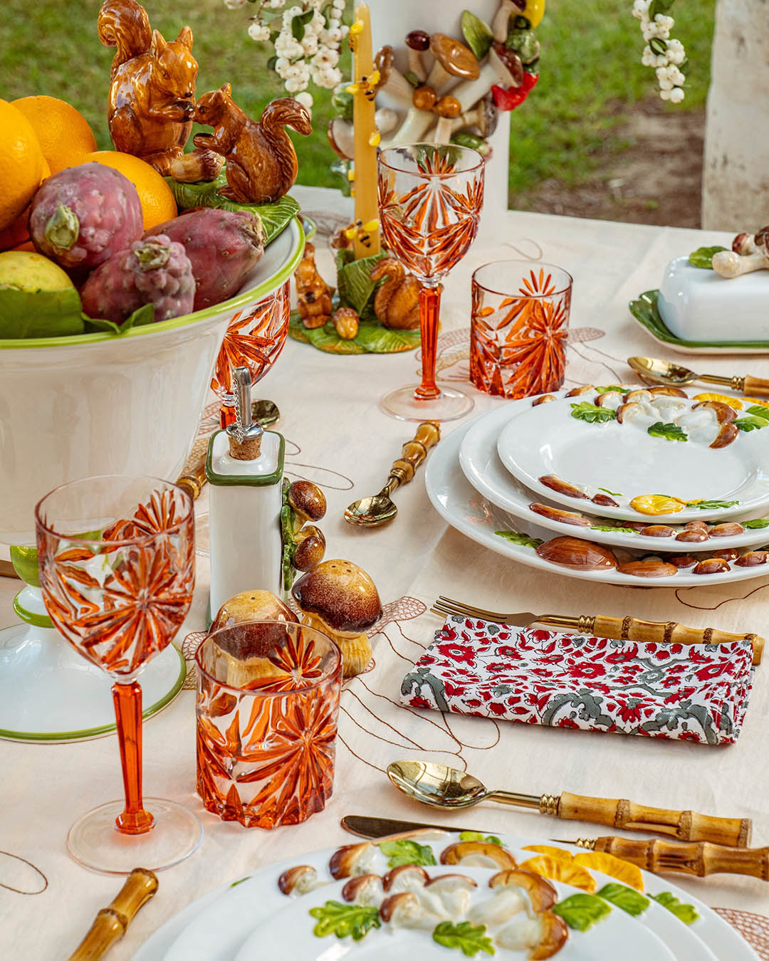 Autumnal table setting with orange cut-crystal glasses, patterned ceramic plates, bamboo-handled cutlery and fruit-filled bowl centrepiece