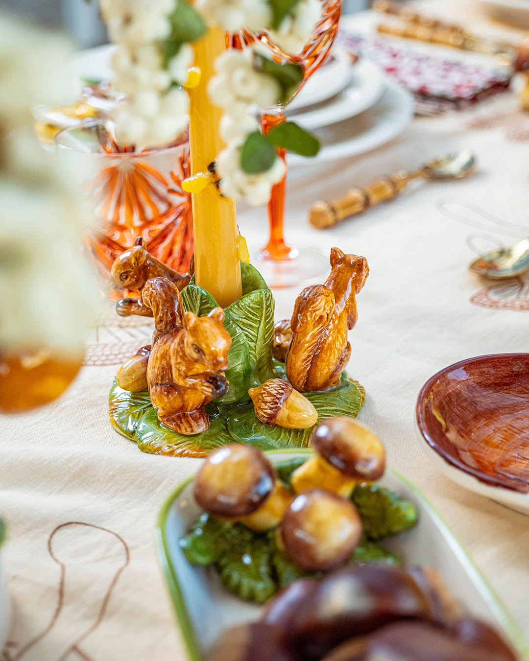 Ceramic squirrel candle holder with a yellow taper candle and decorative mushrooms on a festive table setting