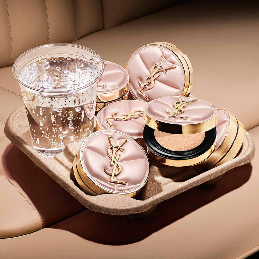 Astucci cushion trapuntati rosa YSL sistemati in un portabicchieri accanto a un bicchiere di acqua frizzante fresca.