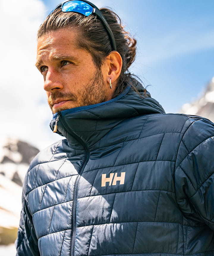 Man wearing a navy Helly Hansen quilted jacket against a mountain backdrop.
