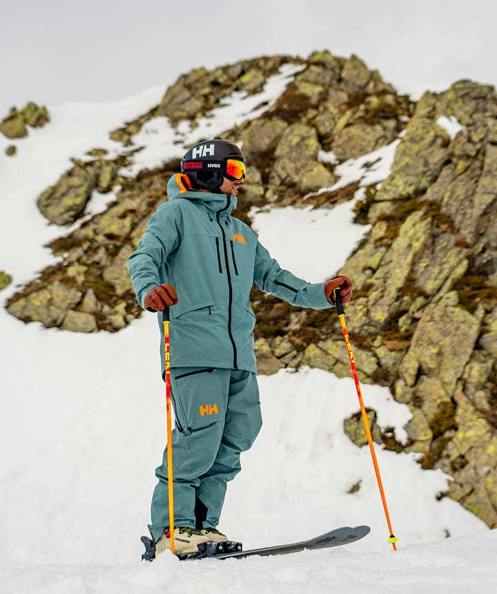Skier wearing a teal Helly Hansen ski outfit on a snowy mountain.