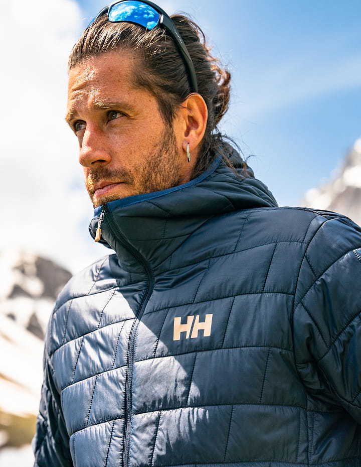 Man wearing a navy Helly Hansen quilted jacket against a mountain backdrop.