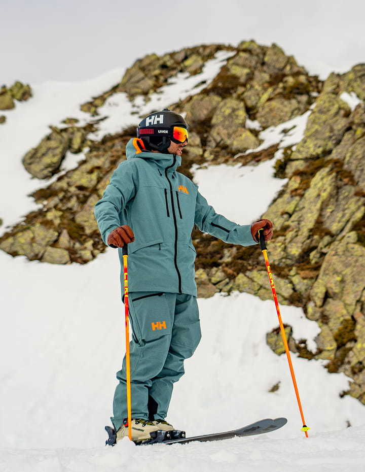 Skier wearing a teal Helly Hansen ski outfit on a snowy mountain.