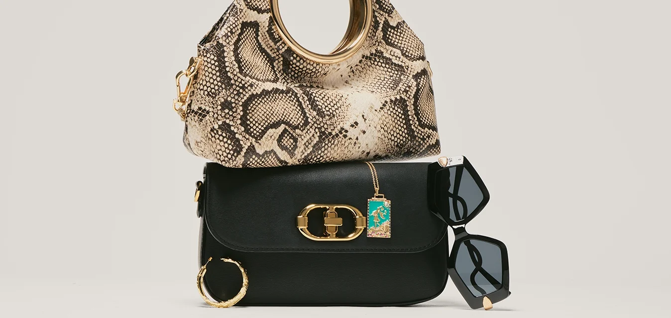 Piccola borsa nera con chiusura dorata, borsa con stampa di serpente e manico rotondo dorato sulla parte superiore, occhiali da sole neri a forma di occhio di gatto e orecchino a cerchio dorato.