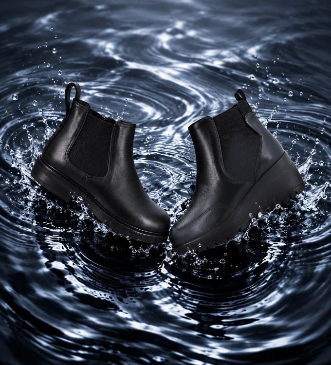Pair of black waterproof Chelsea boots with elastic side panels and platform soles splashing in water