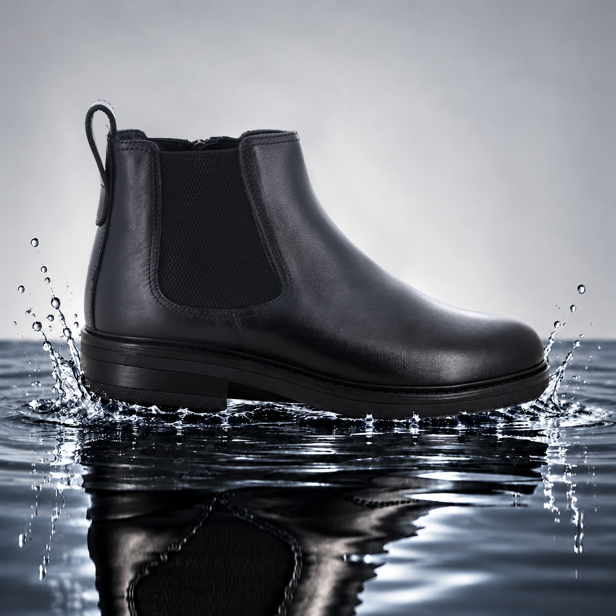 Black leather waterproof Chelsea boot side view splashing in water, elastic ankle panels and pull tab
