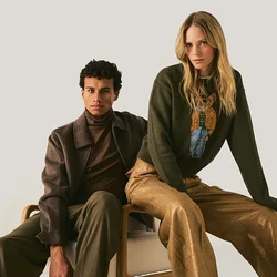 Uomo e donna con abbigliamento autunnale elegante seduti vicini su una panchina davanti a uno sfondo chiaro e semplice.