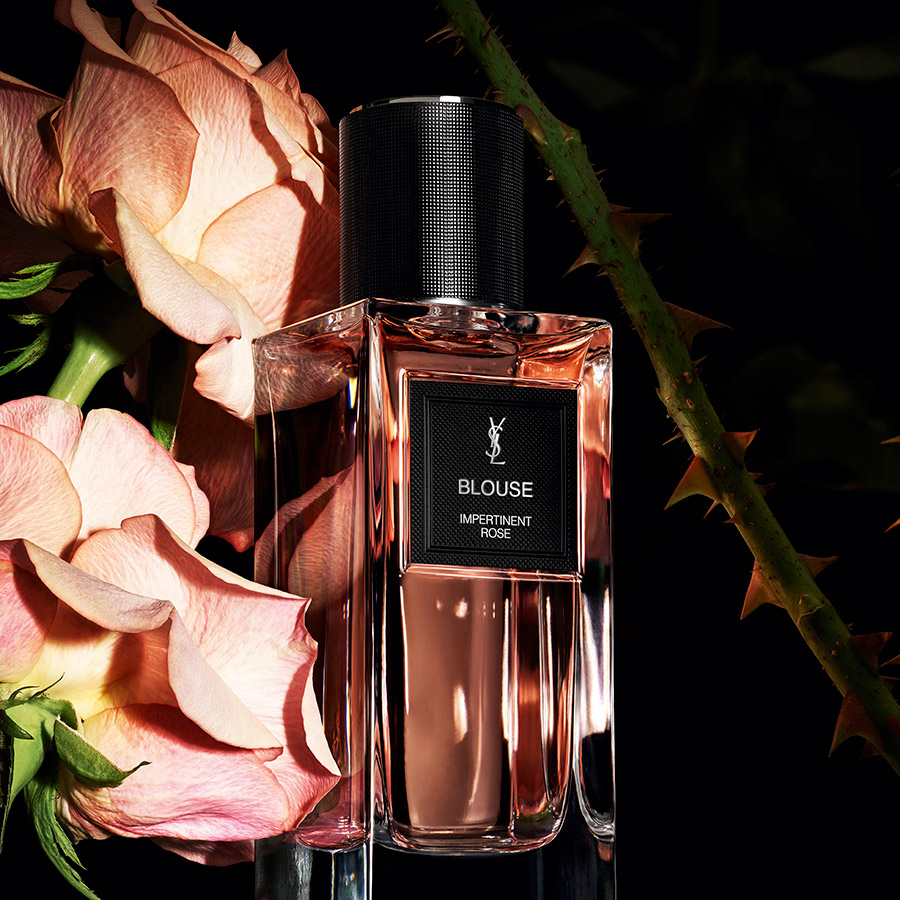 Un flacone di profumo YSL Blouse artisticamente disposto con morbide rose rosa.