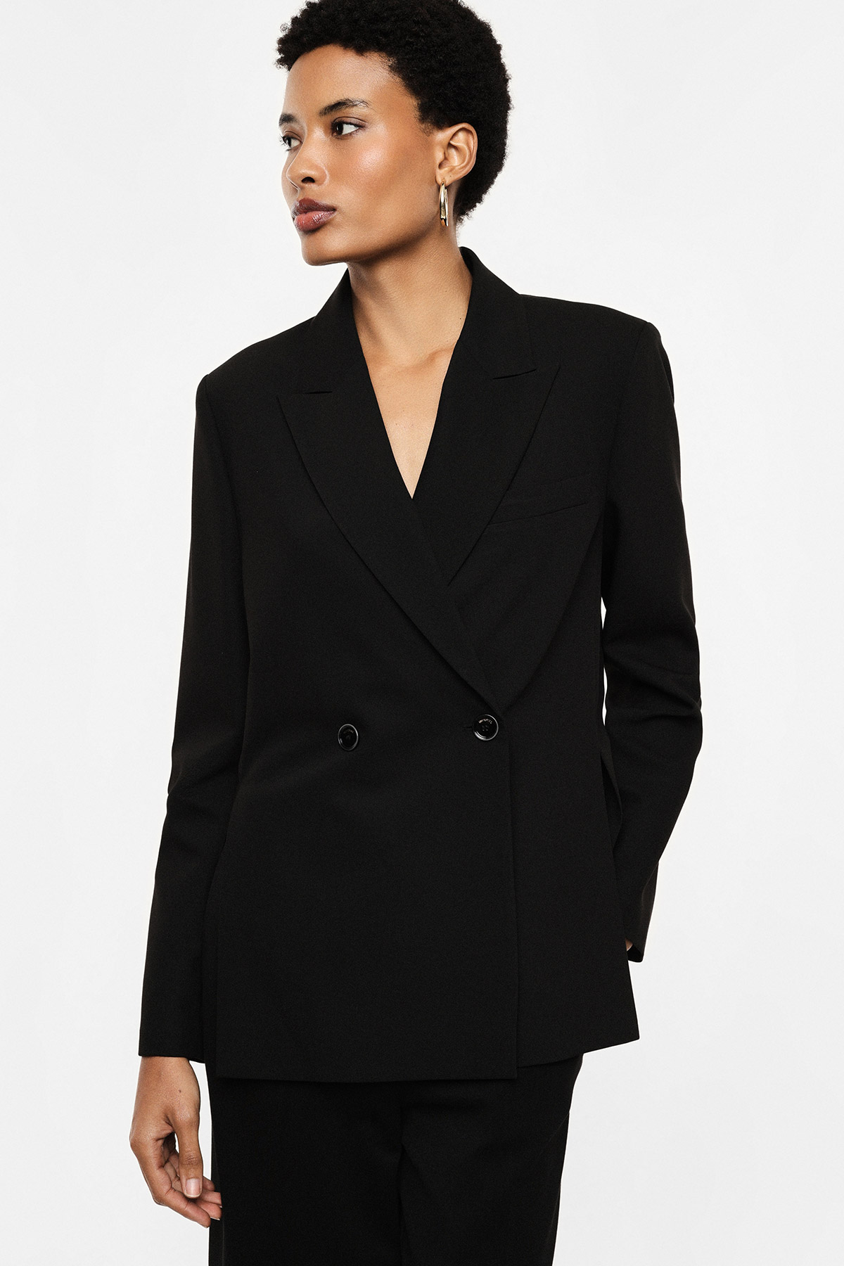 Black double-breasted blazer and matching trousers on a female model against a white background, three-quarter view looking left