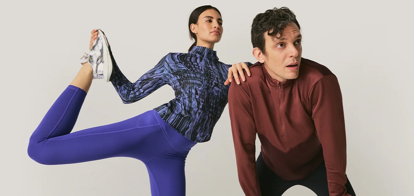 Donna con abbigliamento sportivo blu che allunga una gamba dietro mentre un uomo con una maglia rossa a maniche lunghe si piega in avanti appoggiando le mani sulle ginocchia.