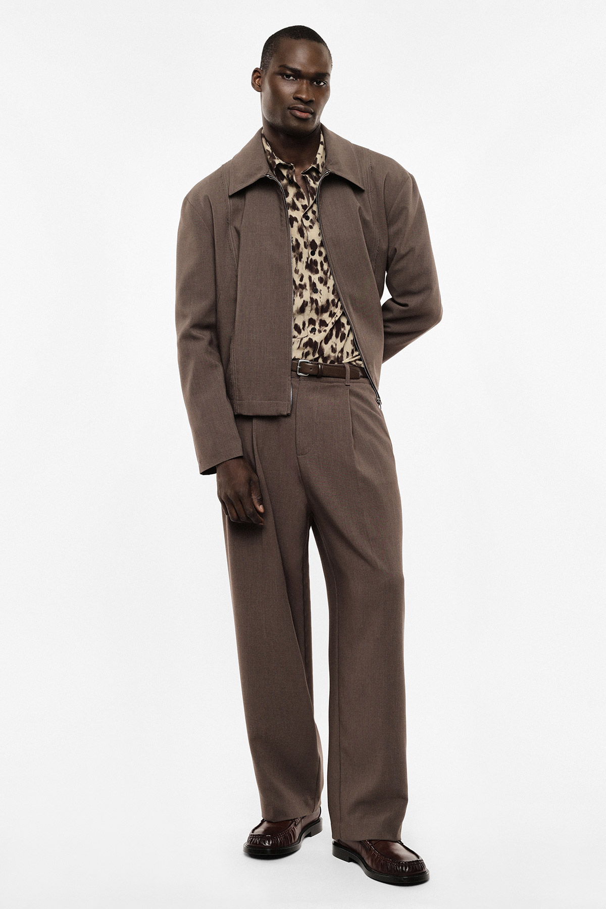 Male model wearing brown tailored jacket and trousers with leopard-print shirt, standing pose