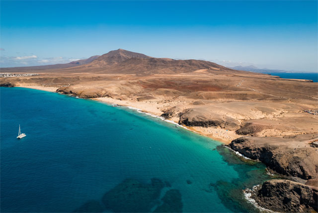 Sunny beach with cliffs and turquoise water.