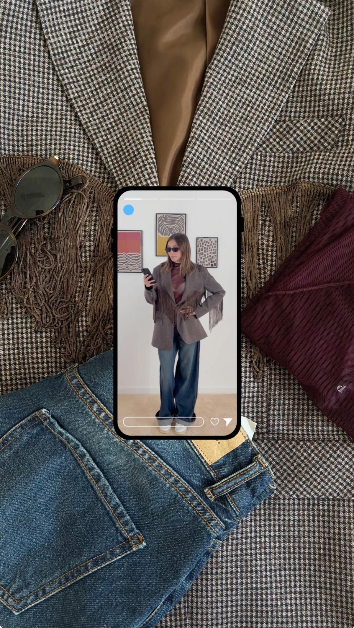 Flatlay of women's outfit — checked blazer, fringed scarf, burgundy top, blue jeans and sunglasses; phone displays woman wearing blazer and wide‑leg jeans