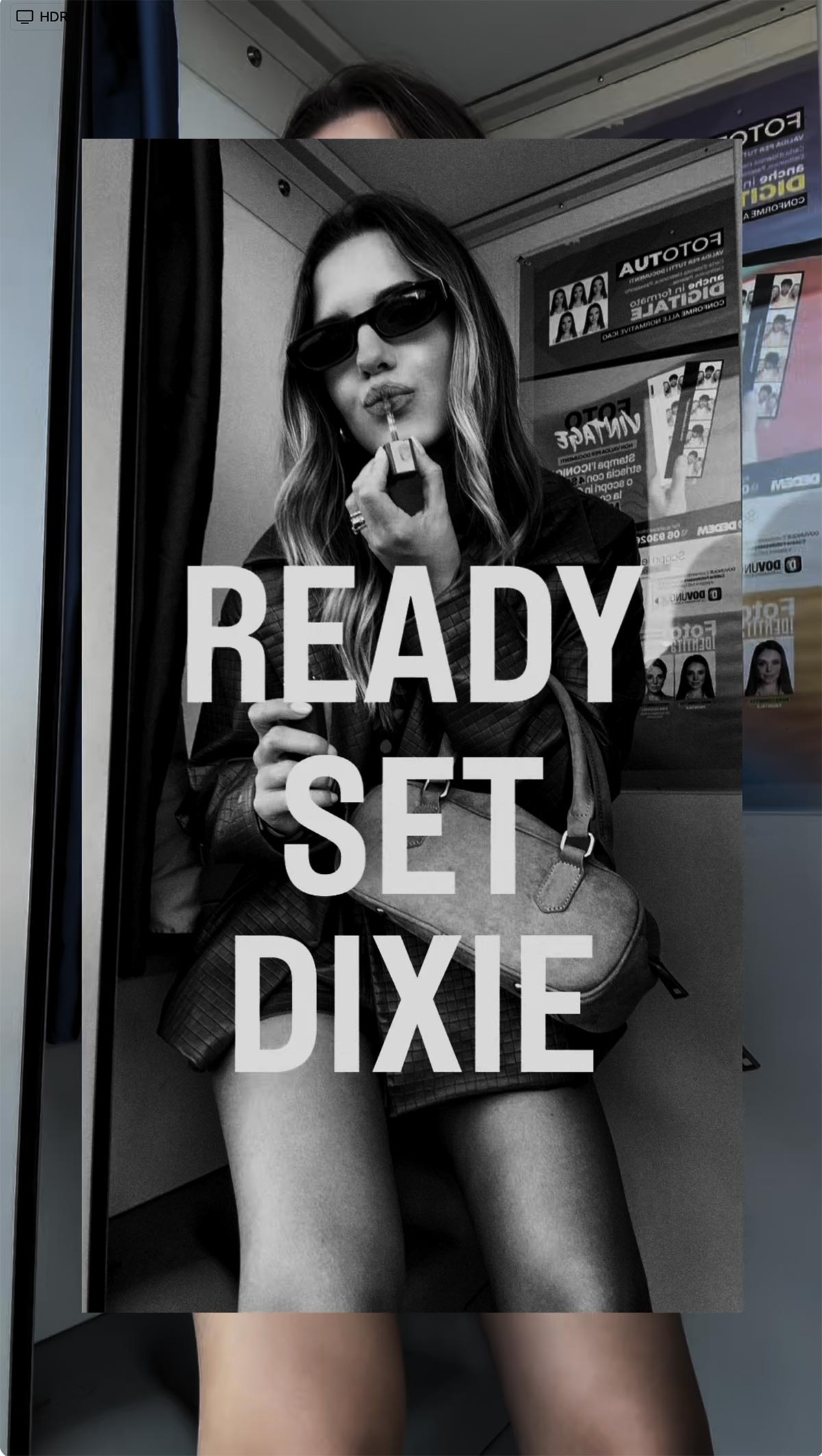 Black-and-white photo of a woman in sunglasses applying lipstick while seated with a handbag; bold text overlay "READY SET DIXIE"