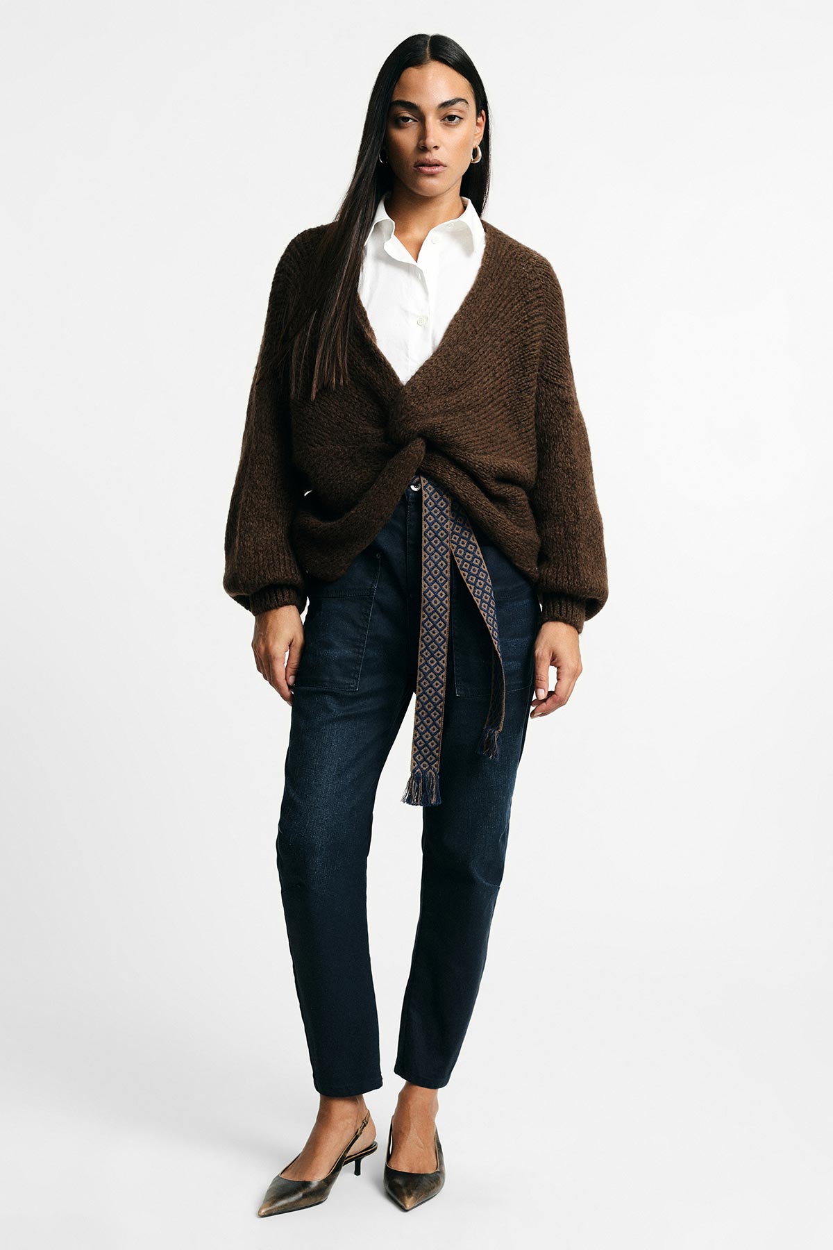 Woman modelling brown chunky wrap cardigan with patterned tie, white shirt, dark tapered jeans and pointed heels, standing front-on