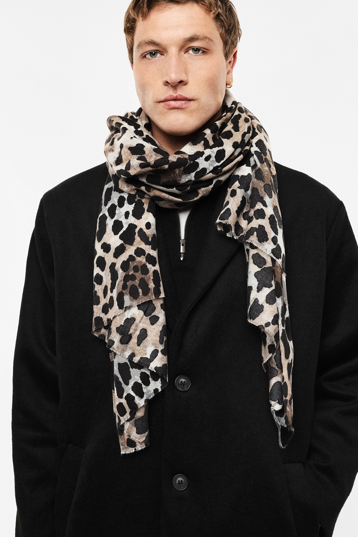 Young man wearing leopard-print scarf draped over black coat in studio portrait — men's winter fashion accessory