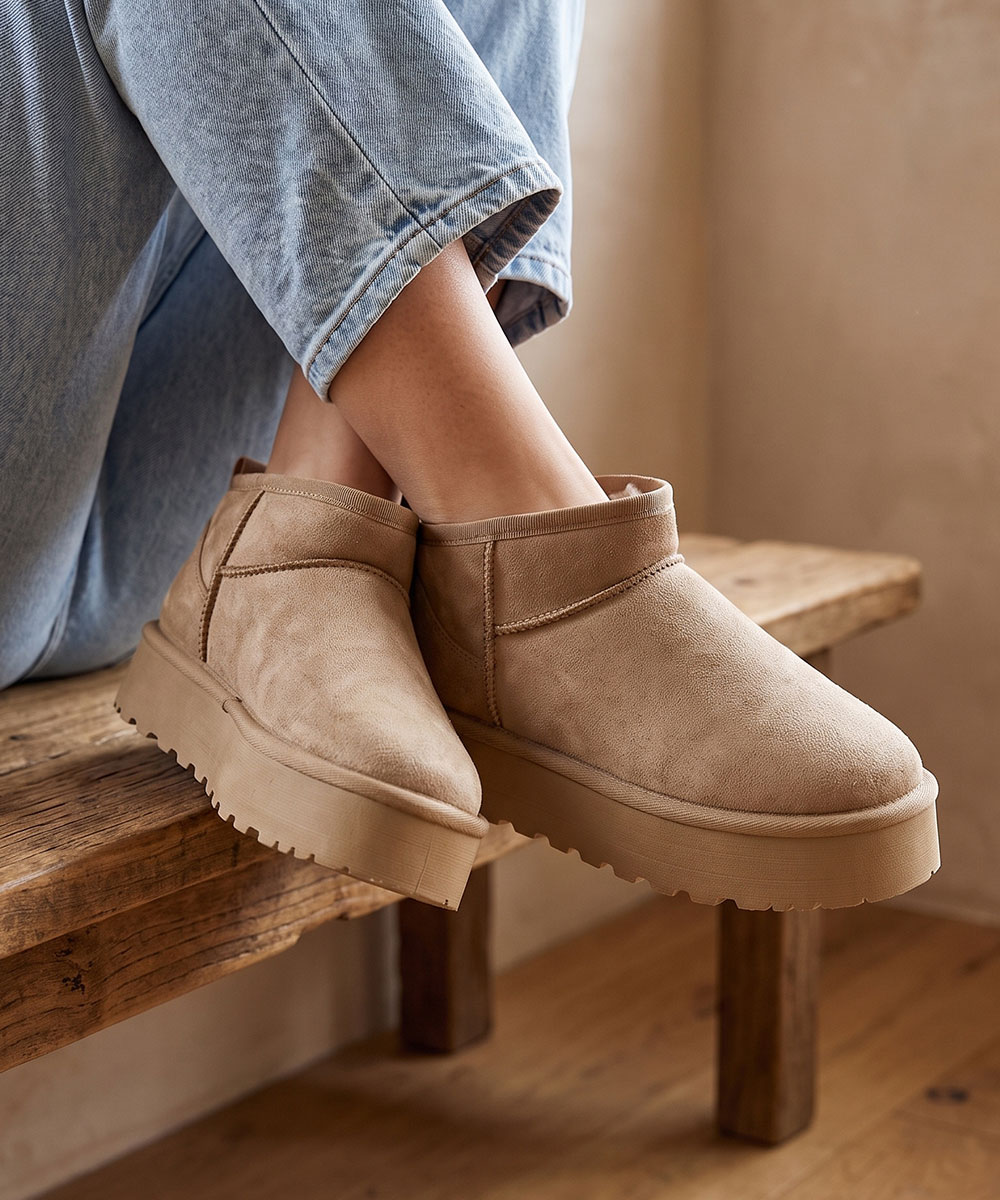 Beige suede platform ankle boots on feet, worn with cuffed light-blue jeans, cosy winter footwear on a wooden bench