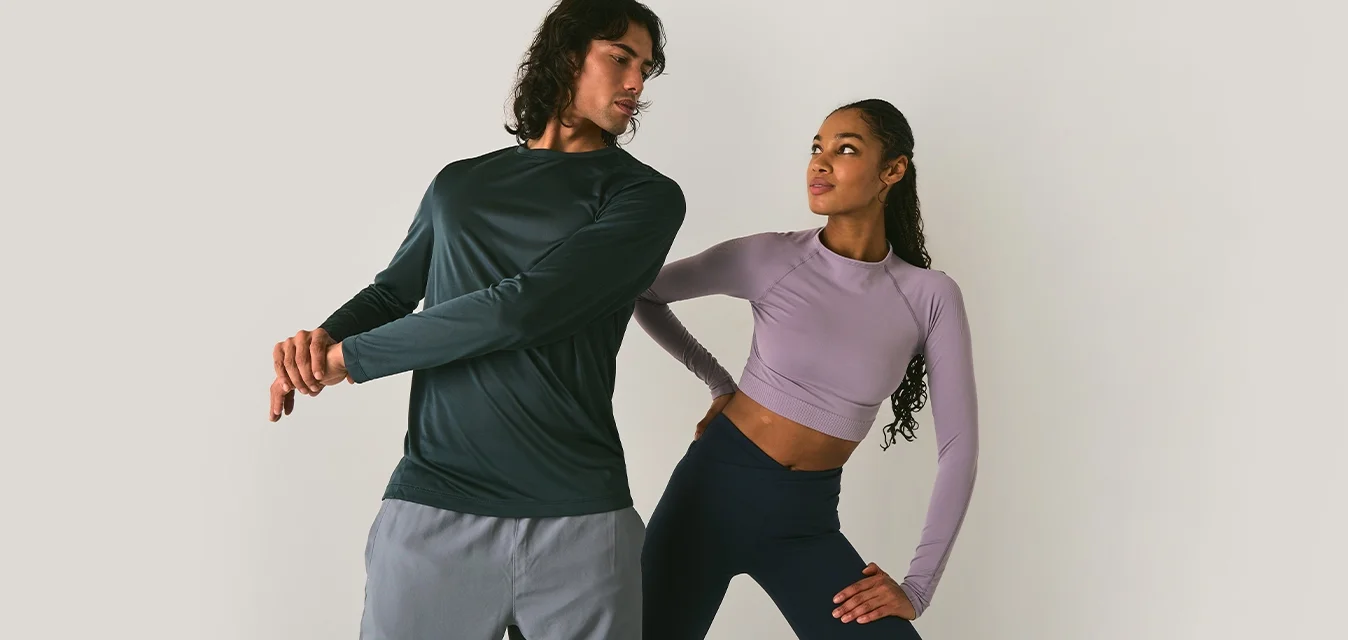 Due persone in abbigliamento sportivo che si stanno allungando; l'uomo tende il braccio attraverso il petto mentre la donna si piega di lato con una mano sul fianco.