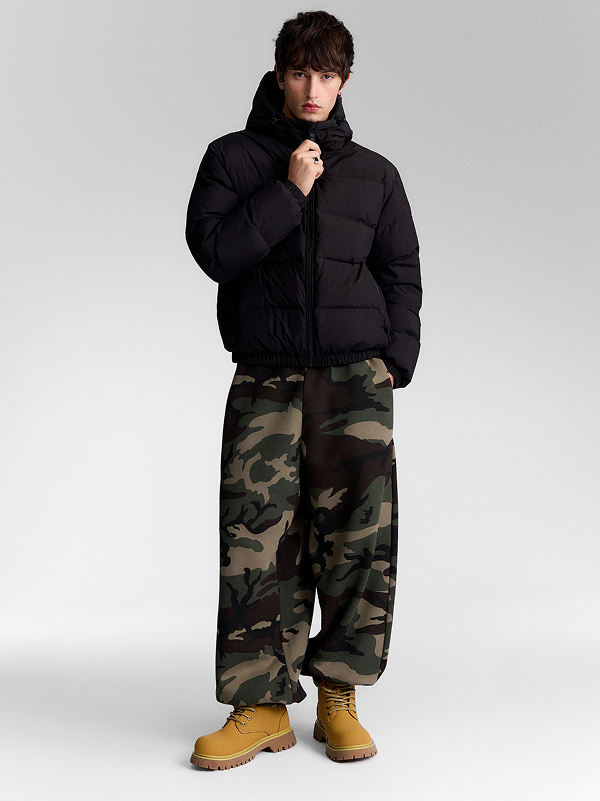 Uomo con piumino nero, pantaloni camouflage e scarponcini gialli.