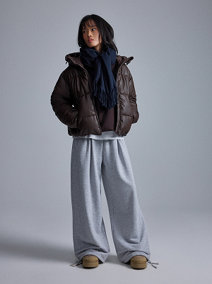 Donna con piumino marrone, sciarpa blu navy e pantaloni larghi grigi.