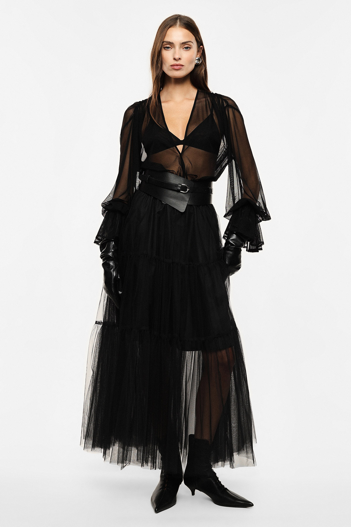 Woman modelling sheer black long-sleeve tulle dress with wide leather belt, black gloves and ankle boots on white background