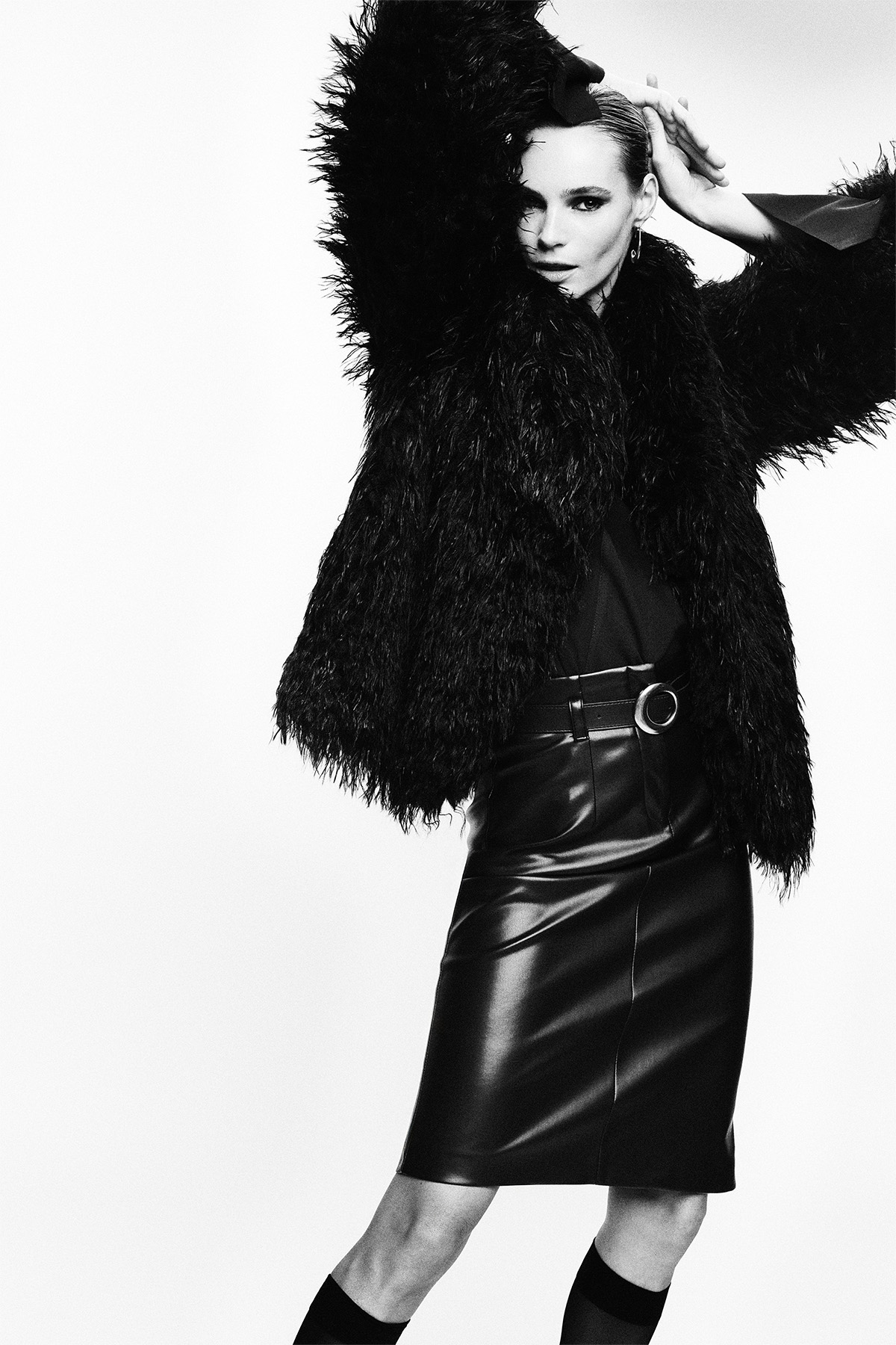 Black-and-white fashion portrait of a model posing in a faux-fur jacket and high-waisted leather pencil skirt, studio shot