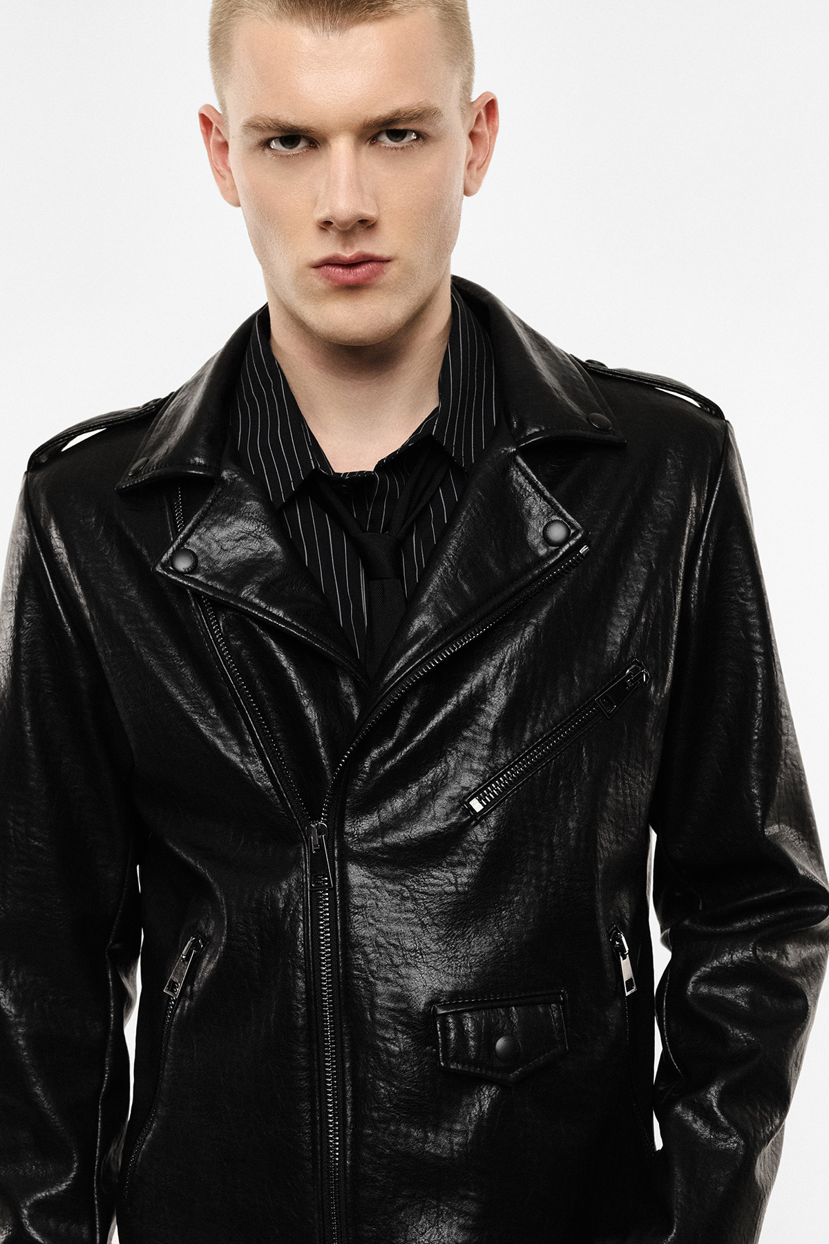 Young man in black leather biker jacket and black shirt with serious expression, studio portrait