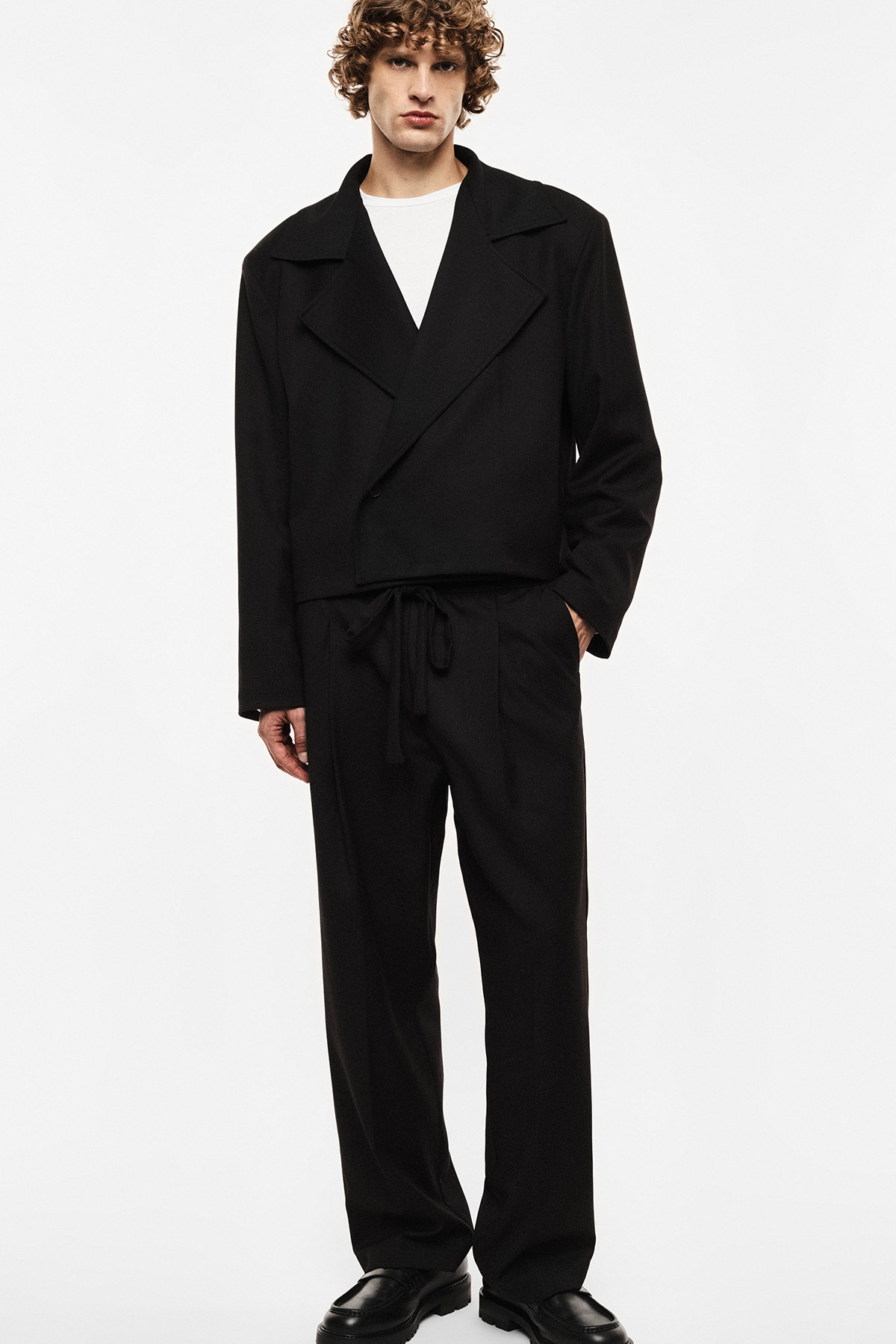 Male model wearing men's black cropped blazer and relaxed drawstring trousers with white T‑shirt and black loafers
