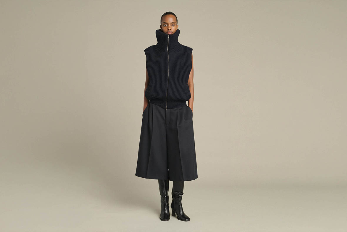 Model wearing black sleeveless high‑neck zip knit vest, wide culotte trousers and black knee‑high boots on neutral background
