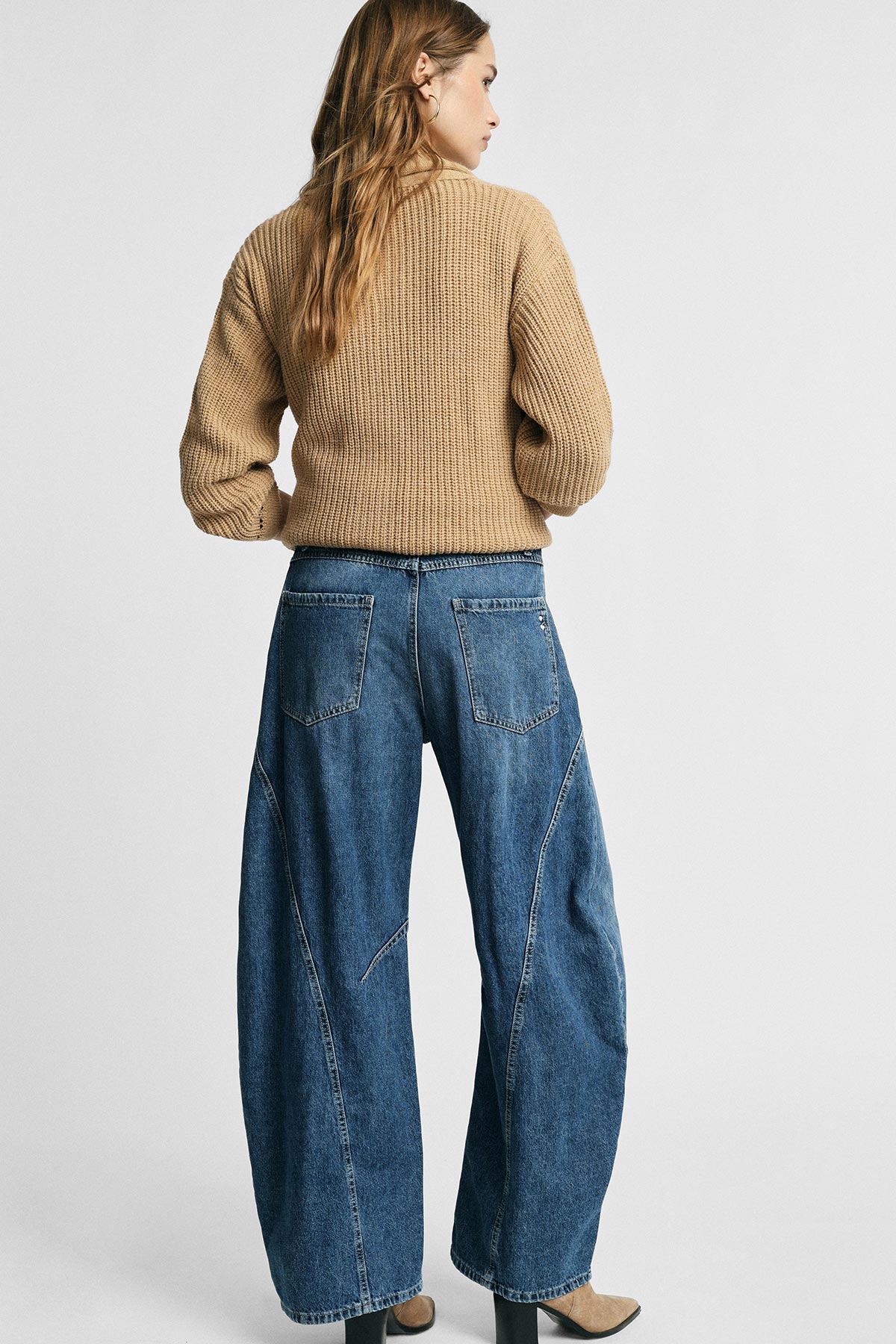 Back view of model wearing beige knitted sweater and high-waisted wide-leg blue jeans in studio