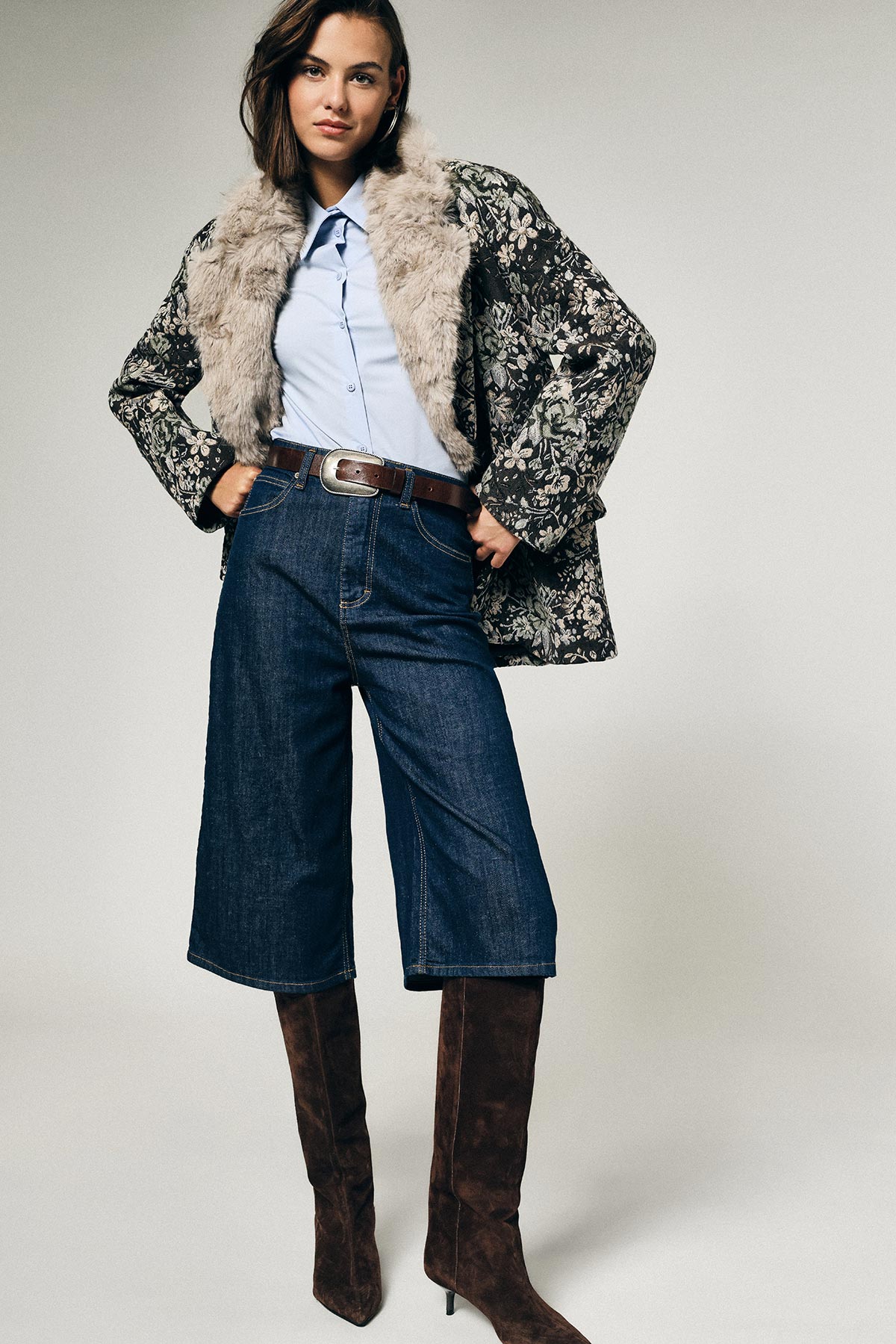 Model wearing fur-collared floral coat, light blue shirt, wide denim culottes and brown knee-high suede boots