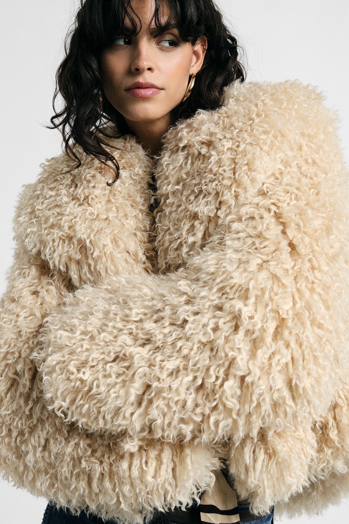 Model in oversized cream shaggy faux‑fur coat, cropped image highlighting coat texture and hoop earring, looking sideways