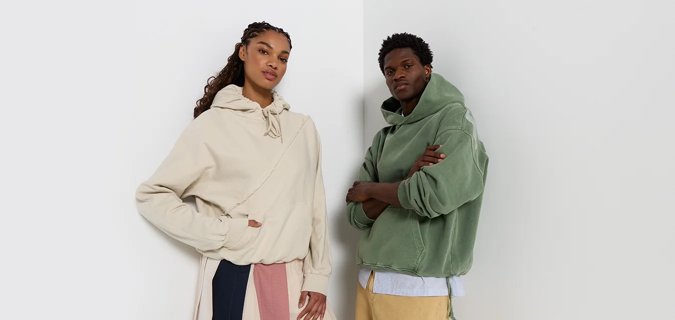 Due felpe con cappuccio si distinguono: una in beige chiaro con tasca frontale e cuciture dettagliate, l'altra in verde tenue con una vestibilità comoda.