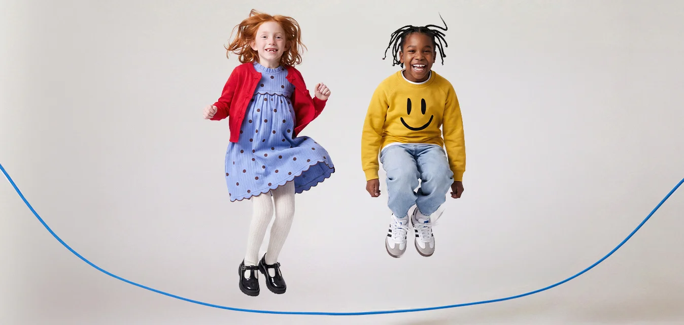 Due bambini che saltano felicemente la corda, una bambina in un vestito blu e un cardigan rosso, e un bambino con un maglione giallo con una faccina sorridente e dei jeans.