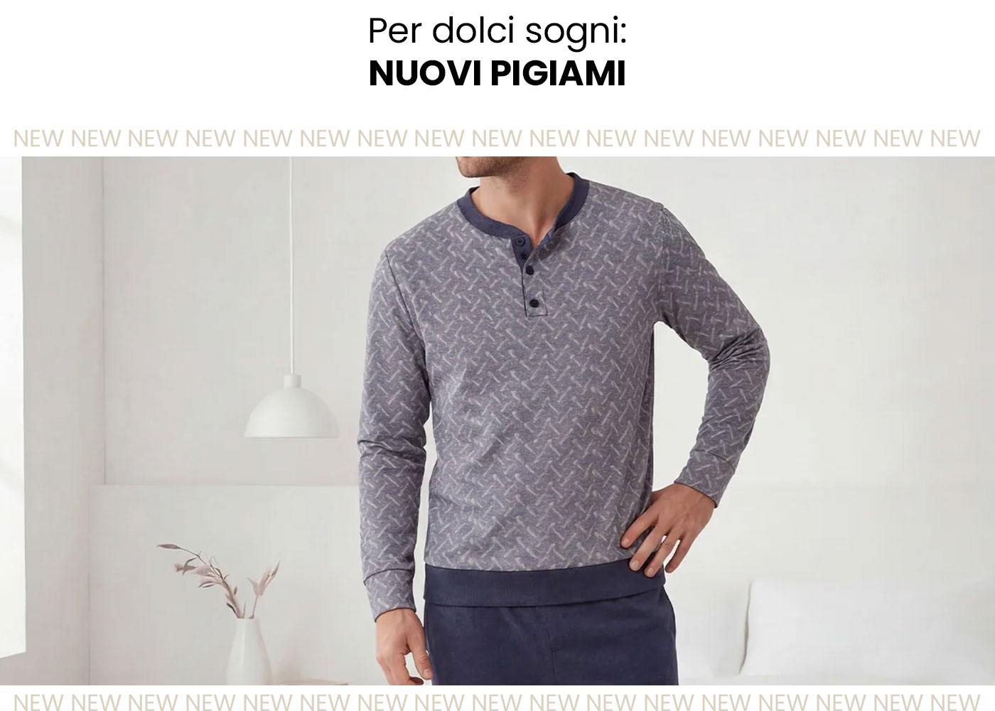 Male model wearing grey patterned long-sleeve henley pyjama top and navy pyjama bottoms in a minimalist bedroom setting