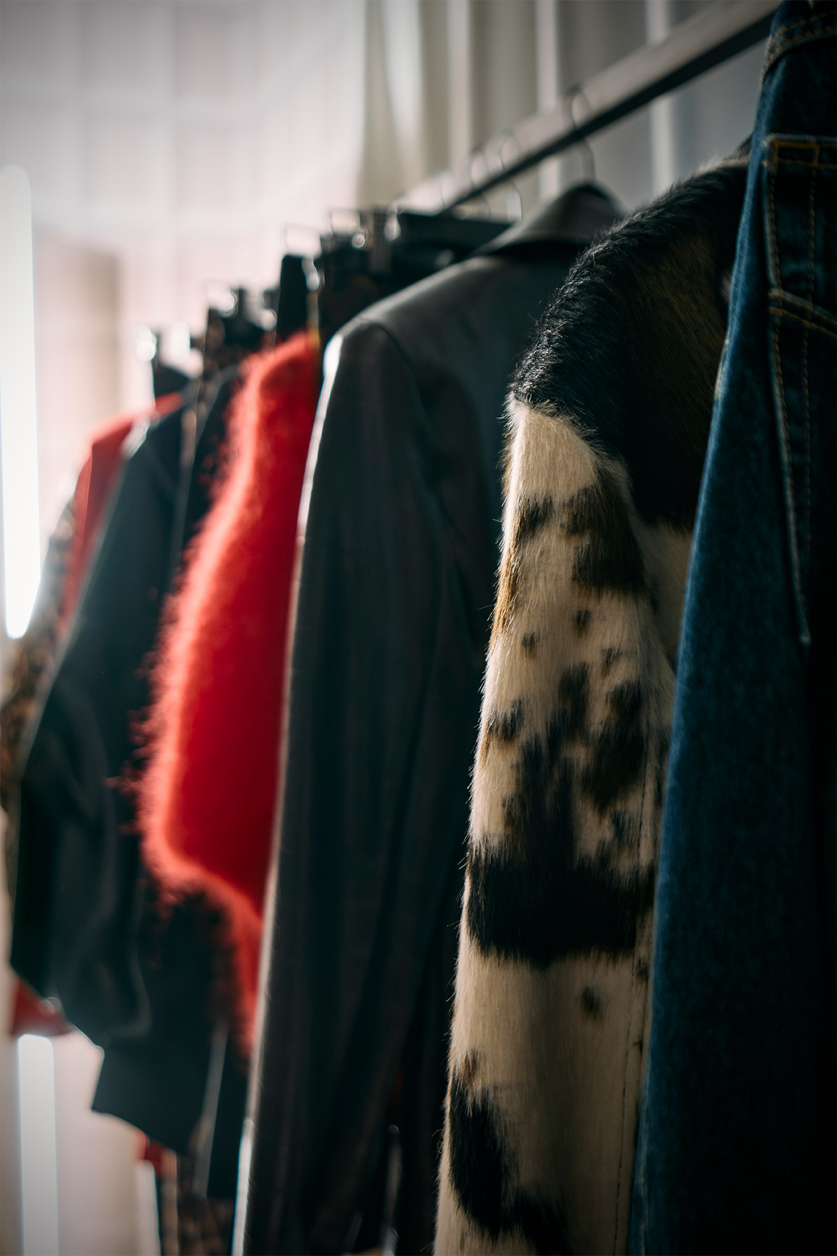Row of coats on a clothing rack including a spotted fur coat, red fuzzy jacket and dark leather and denim outerwear
