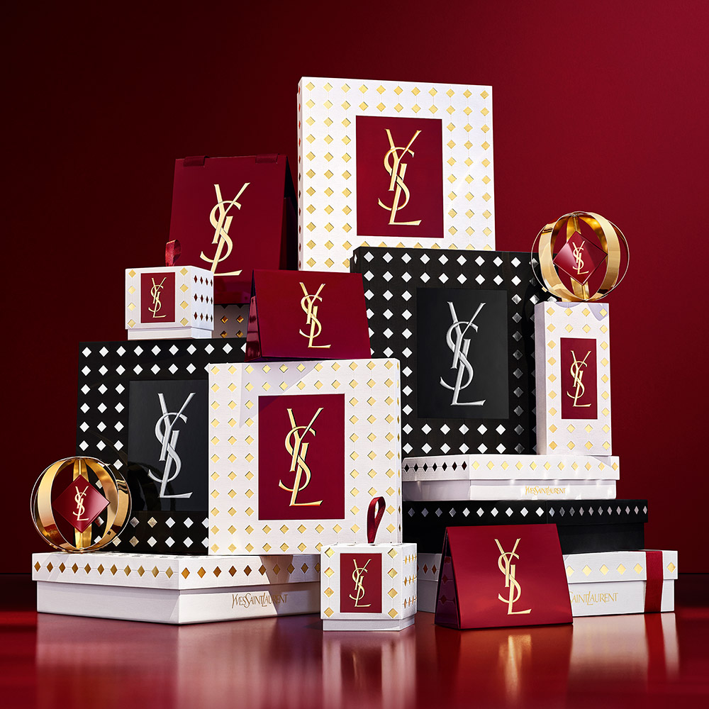 Confezioni regalo YSL Beaut&eacute; rosse, bianche e nere con dettagli dorati, disposte su uno sfondo rosso intenso.