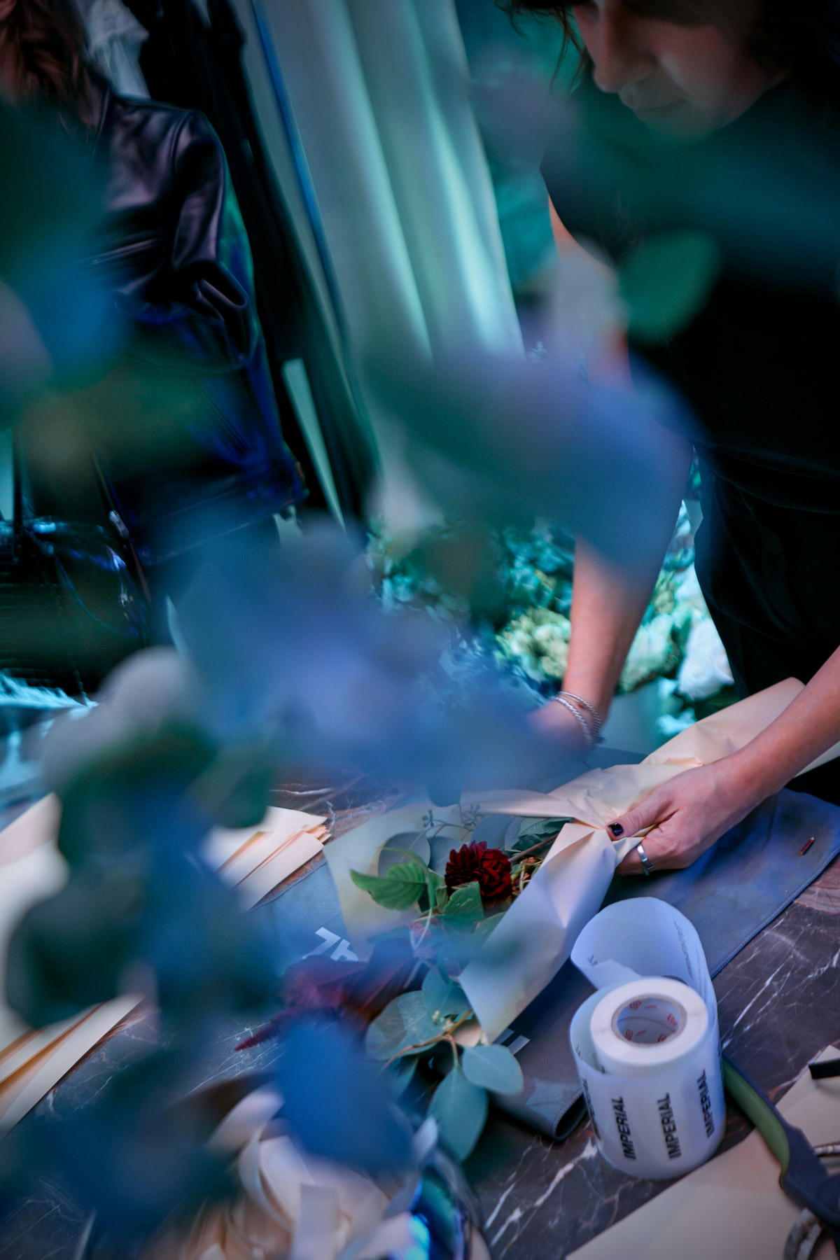Florist wrapping a hand-tied bouquet with eucalyptus and red flowers on a workbench, tools and tape visible