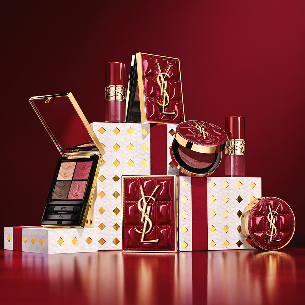 Confezioni regalo e prodotti make-up YSL Beaut&eacute; disposti su uno sfondo rosso intenso.
