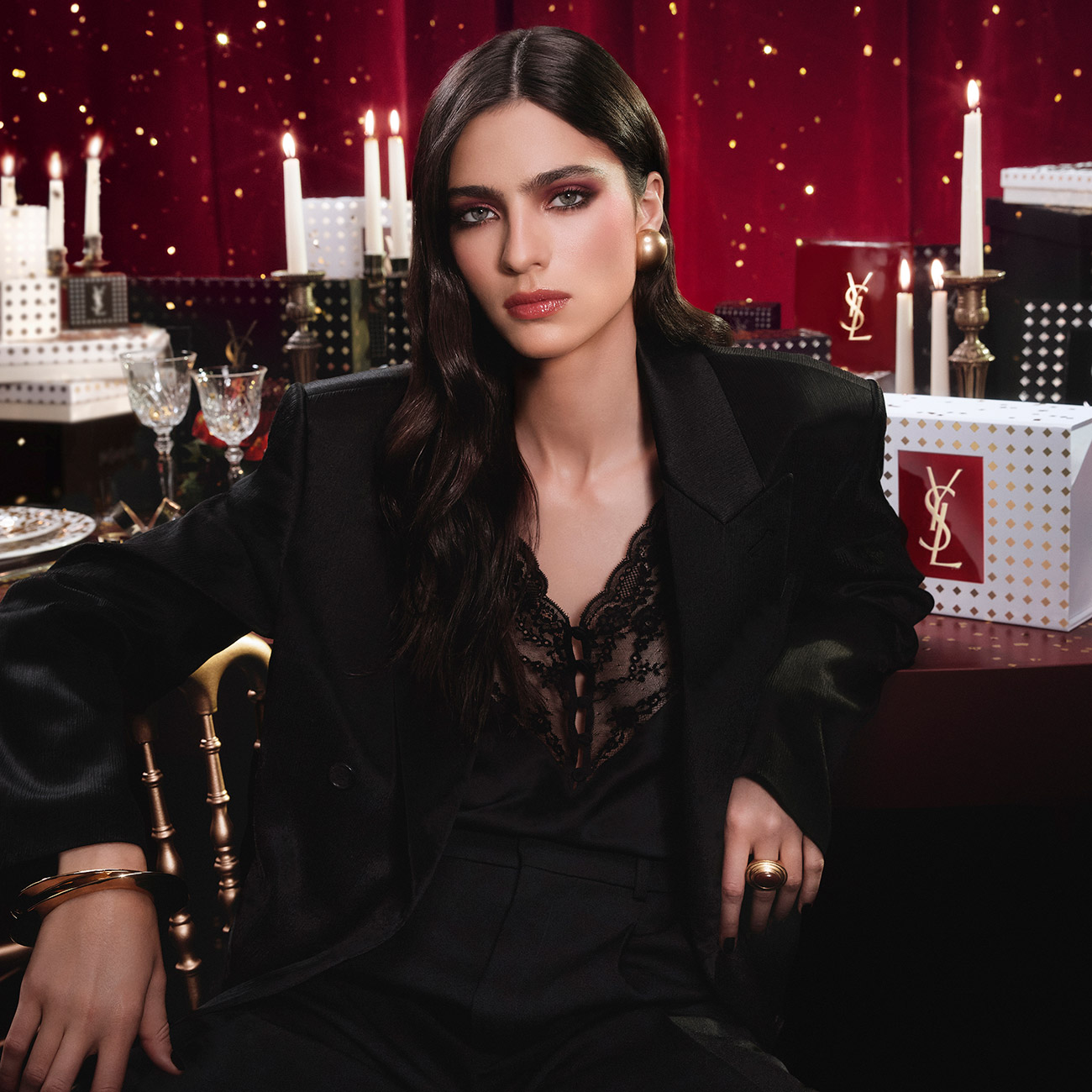 Una donna vestita di nero posa in un&rsquo;atmosfera festiva YSL Beaut&eacute;, tra candele e confezioni regalo.
